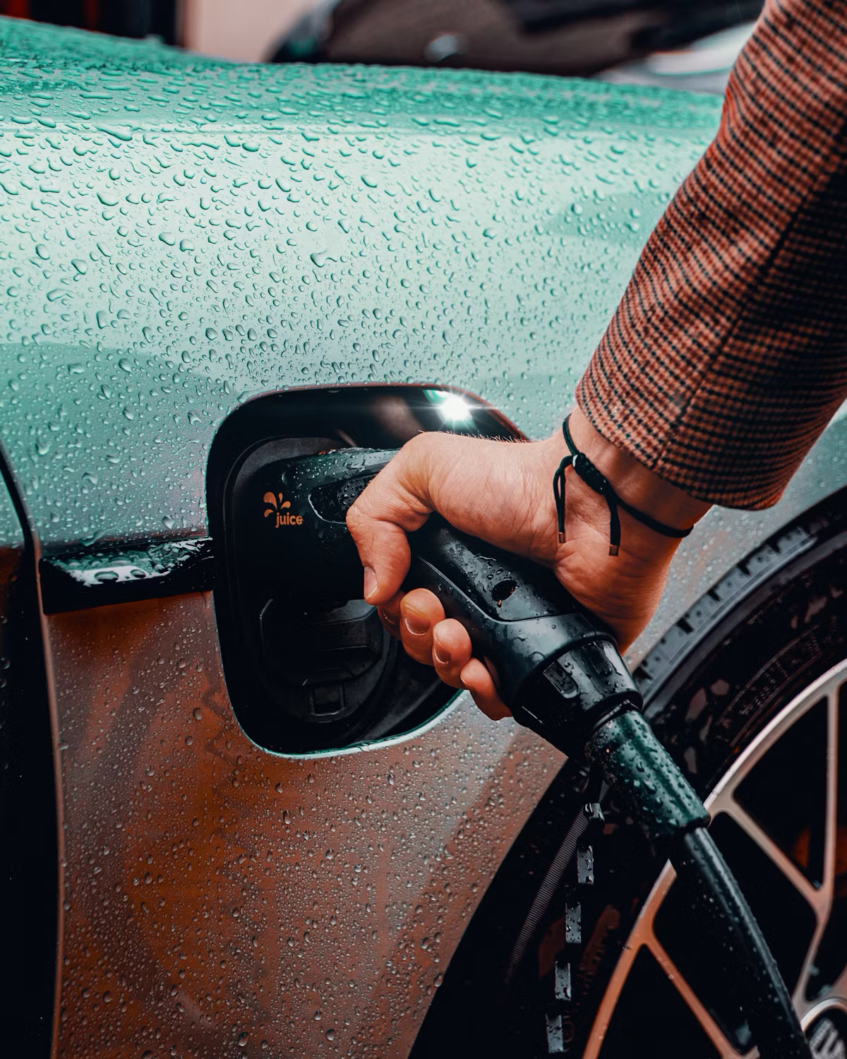 A person plugging a charging connector into an electric vehicle in the rain